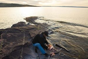 Person cleaning a fish on rocks by the sea.