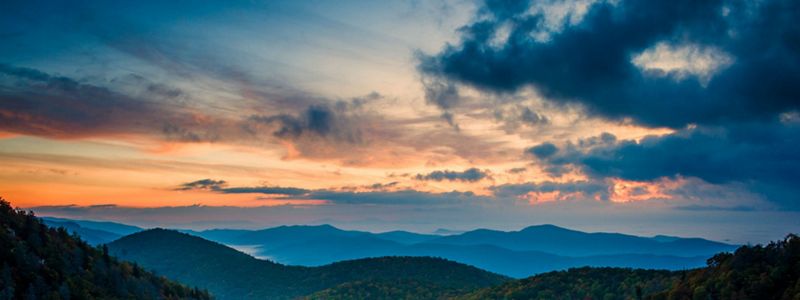 Sweeping view of layers of mountain ranges as the sun sets in the distance.