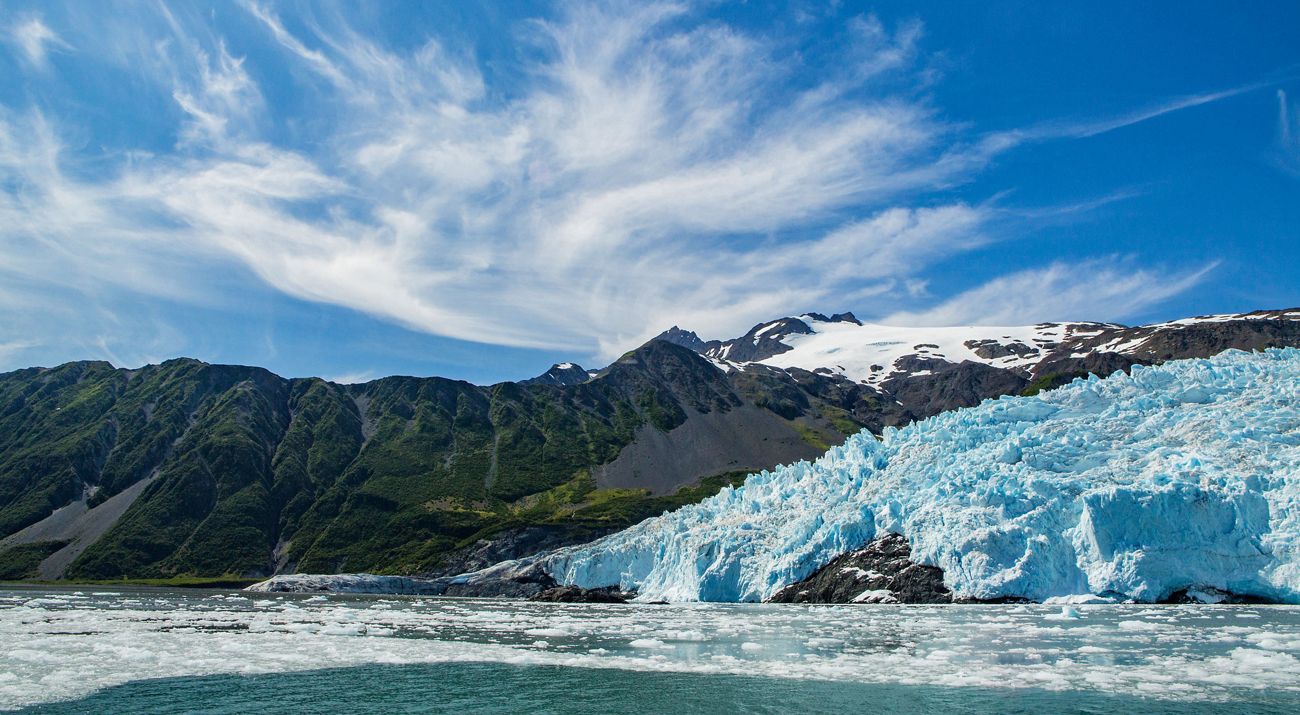 A large, jagged glacier flows down into a body of water framed by mountains.