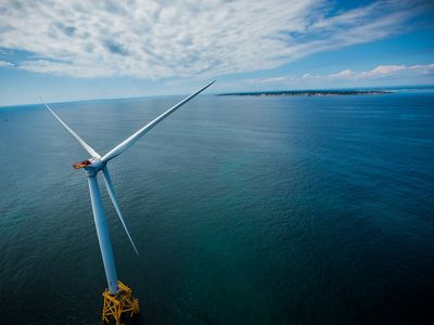 Aerial view of a white wind turbine in the ocean with Block Island in the distance.
