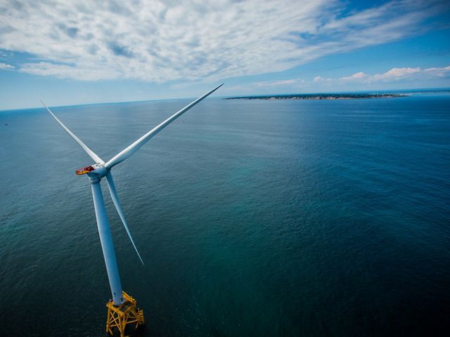 A wind turbine sits in the middle of  a blue ocean.