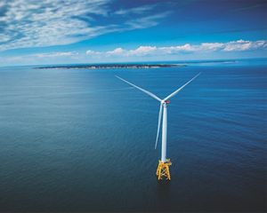 An aerial view of a wind turbine in the ocean, with the coast of Block Island and Rhode Island in the background.