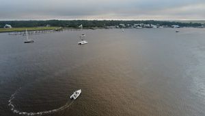 A wide dark river is bordered by boats and a small town at its banks.