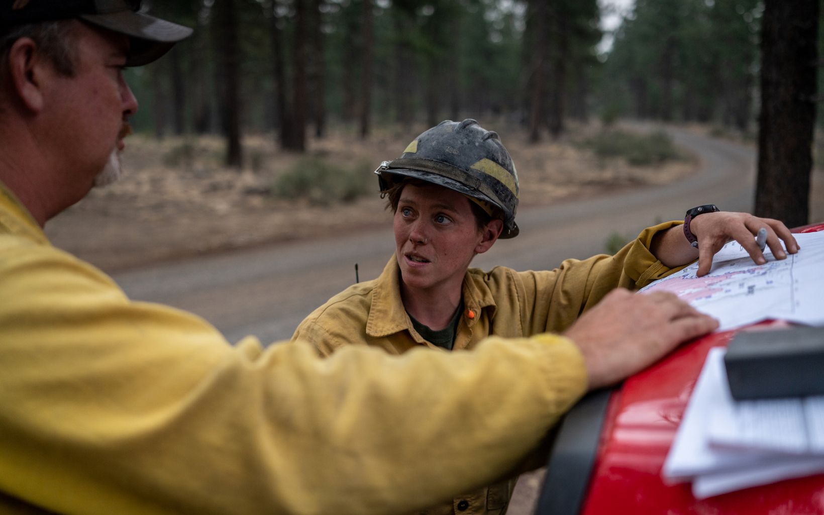 TNC Oregon Fire Manager Katie Sauerbrey looks at maps on the hood of a red truck and discusses fire management strategies with another TNC Fire Crew member. 