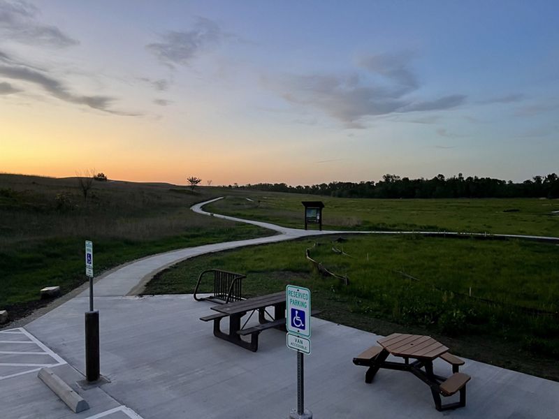 The sun sets over native prairie grasses and paved trails.