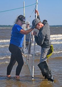 Two people stand along a shoreline to take measurements.