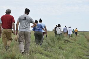 hombres y mujeres caminando en linea entre el pasto.