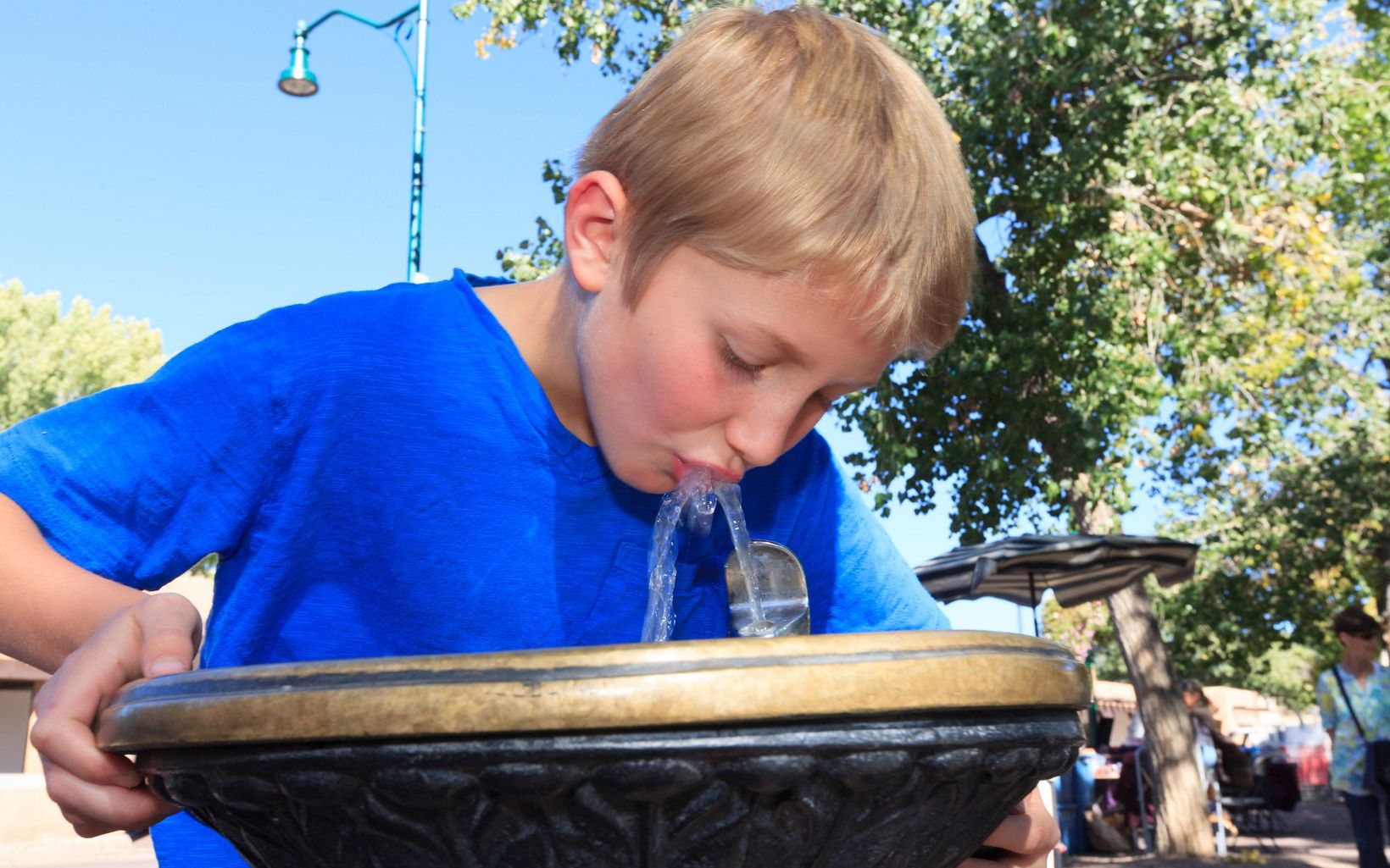 Boy in bright blue t-shirt drinks from water fountain.