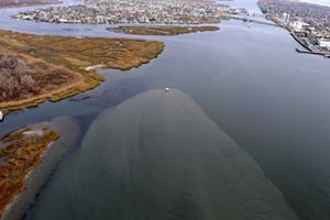 Aerial view of discolored water spreading through wetlands and channels after storm damage, showing pollution dispersing through the surrounding bays.