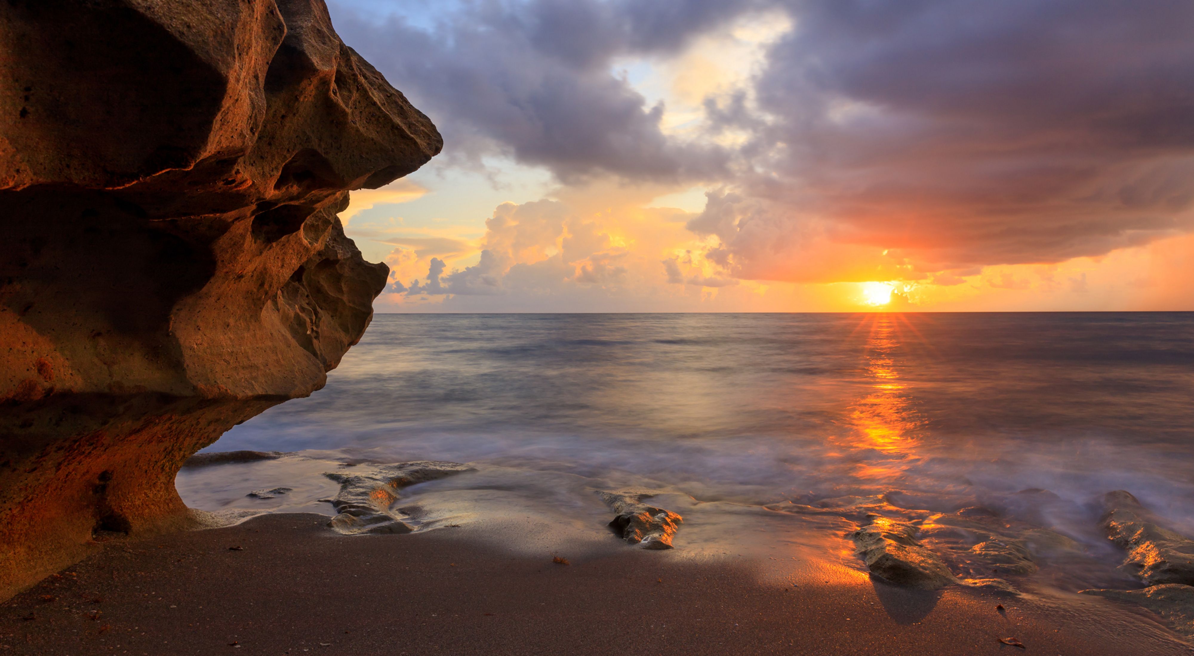 Sunrise over the ocean, with a large rock formation in the left foreground.