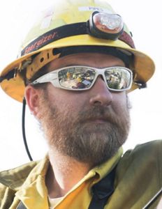 Headshot of Bryn Pipes with a yellow helmet and jacket with a headlamp.