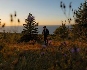 A man in a baseball cap walks along a trail with Lake Superior in the background.