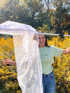 A person smiles holding a butterfly net towards the camera. 