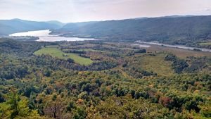 Landscape view from the top of a mountain showing a wide forested valley on the edge of a body of water.