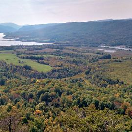 Landscape view from the top of a mountain looking down at a wide forested valley on the edge of a body of water.