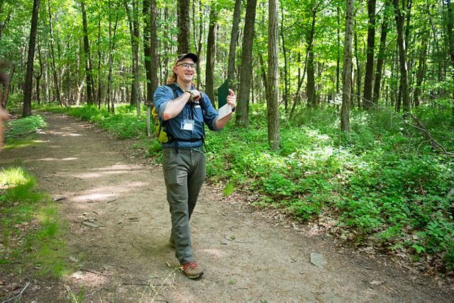 A man in a hat walks through a forest along a dirt trail.