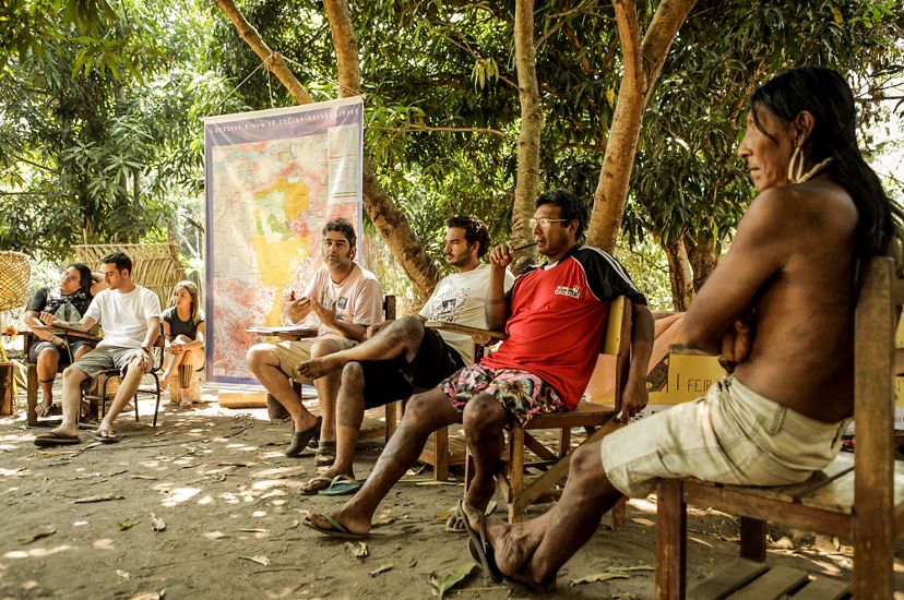 Indigenous men sit in a circle and talk about land management under the shade of trees in Brazil's amazon.