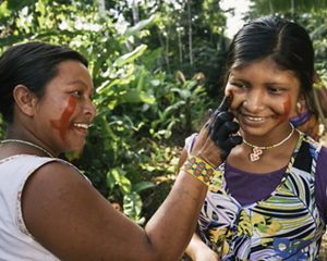 Mulher indígena pinta o rosto de uma outra mulher mais jovem.