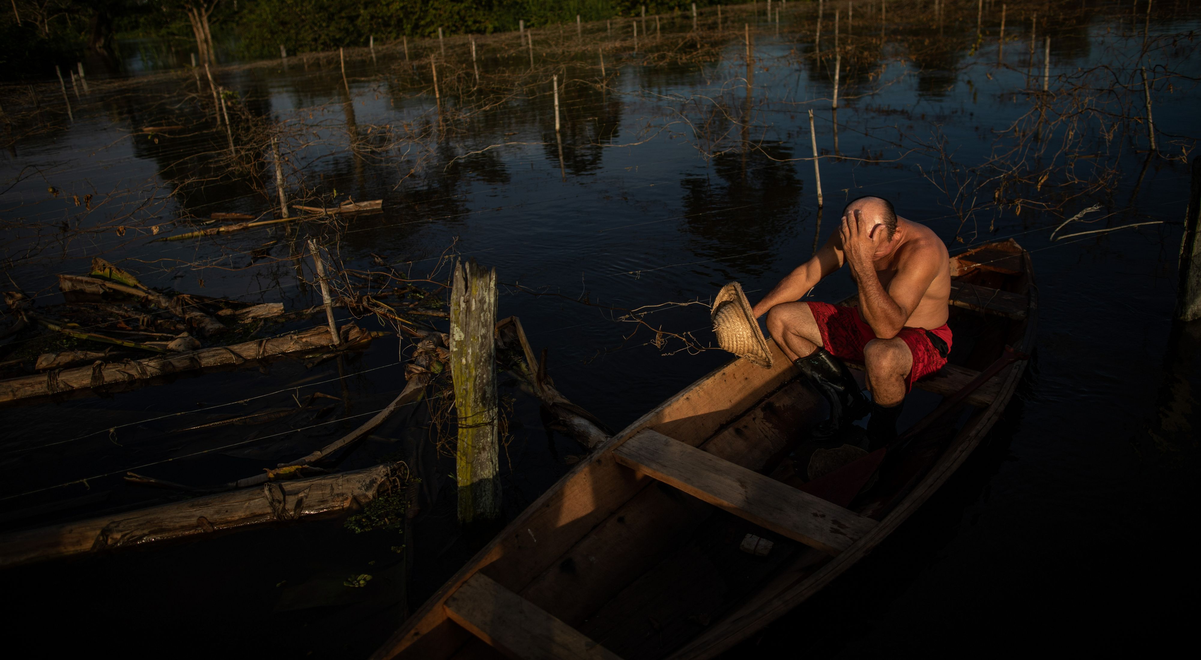  Agricultor sentado com a mão em sua cabeça em um barco lamentando a perda da sua plantação.