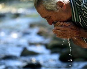 Proprietário rural lava o rosto com água em beira de rio