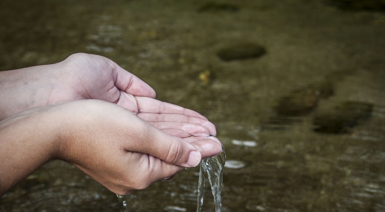 Water falls through two hands that are cupped to hold it.