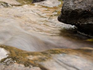 Água correndo próximo a pedras na beira de um rio.