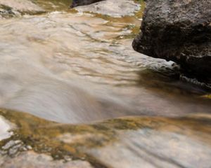 Água correndo próximo a pedras na beira de um rio.