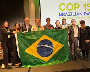 Participantes da mesa de abertura do evento segurando a bandeira do Brasil.