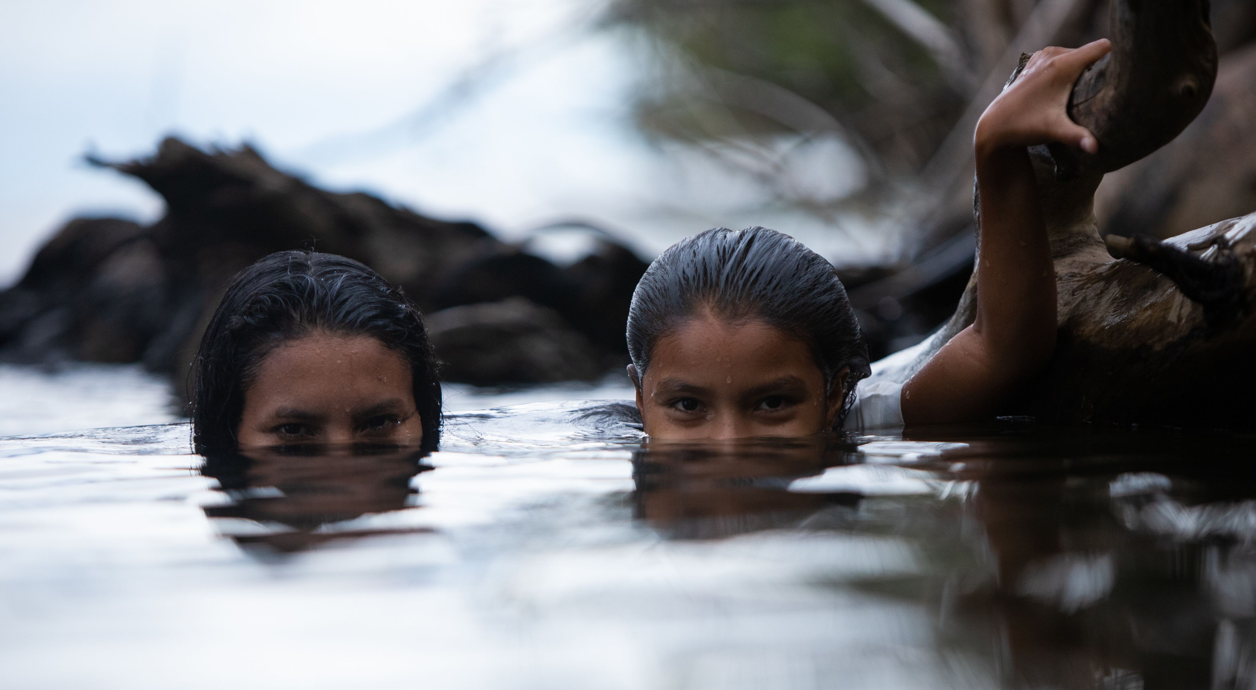 Meninas brincando em rio e olhando para câmera.