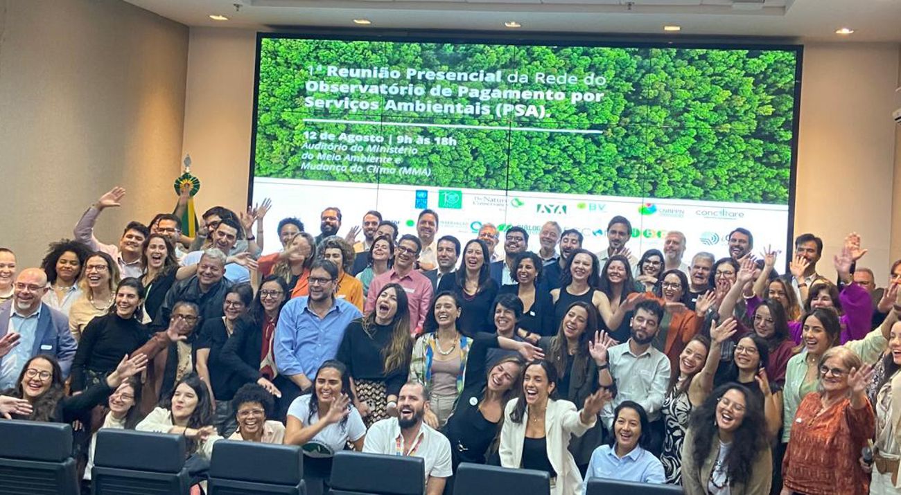 Grupo reunido em auditório para reunião da Rede PSA, com tela ao fundo exibindo data, local e logotipos de instituições.
