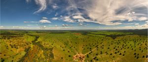 A imagem mostra uma ampla paisagem rural vista de um ponto elevado, provavelmente por drone ou aeronave, capturada em formato panorâmico.