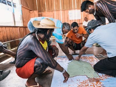 A group of people kneel around maps spread out on a floor.