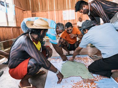 Um grupo de pessoas se ajoelha em volta de mapas espalhados no chão