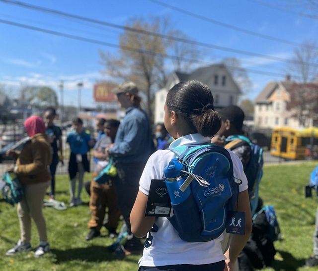 A young girl wearing a backpack observes a group.