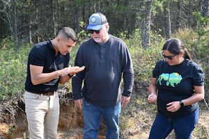 Three people standing in nature and looking at soil.