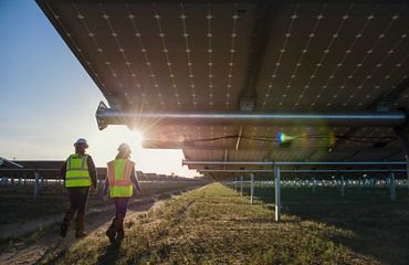 Two workers walk under a solar panel.