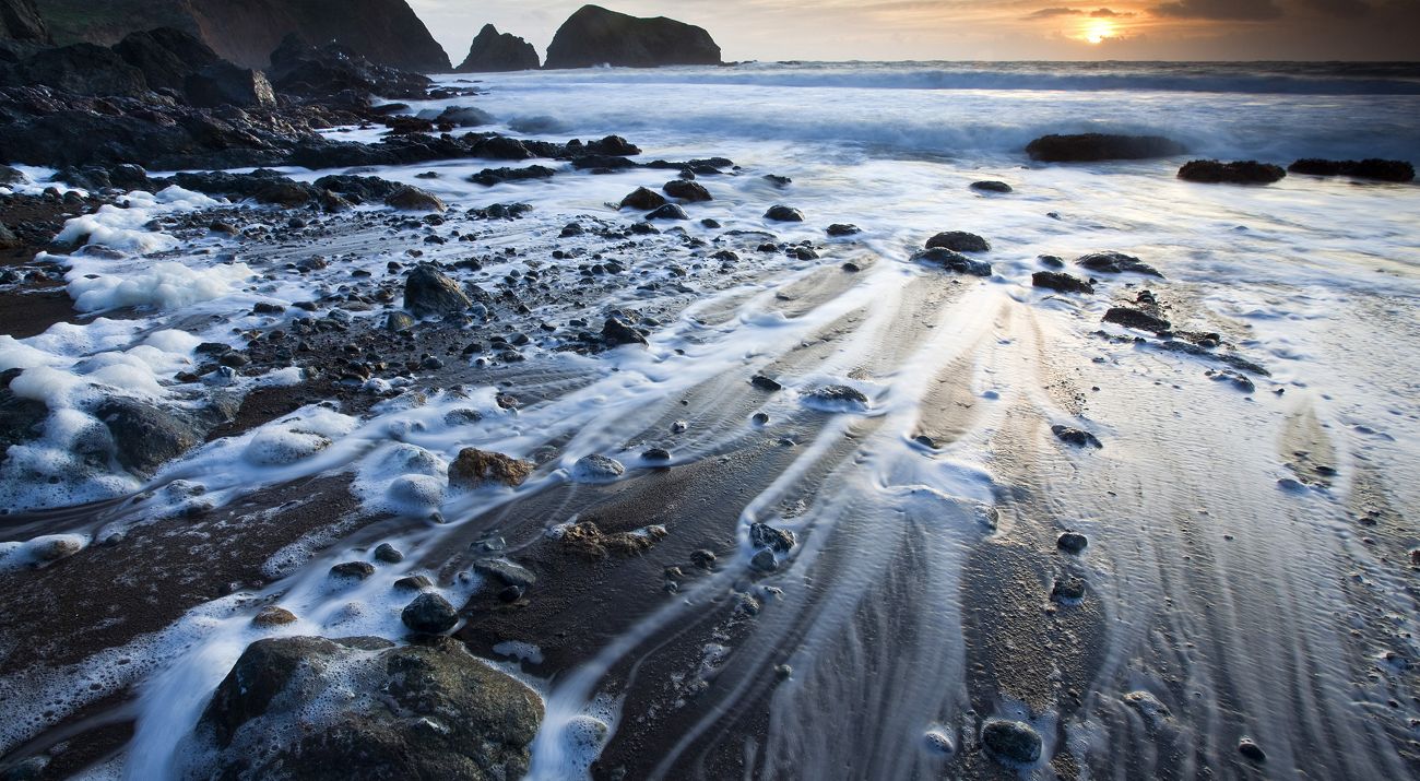 A closeup of a rocky shore with surf along the sand.