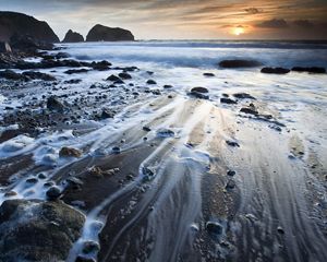 A closeup of a rocky shore with surf along the sand.