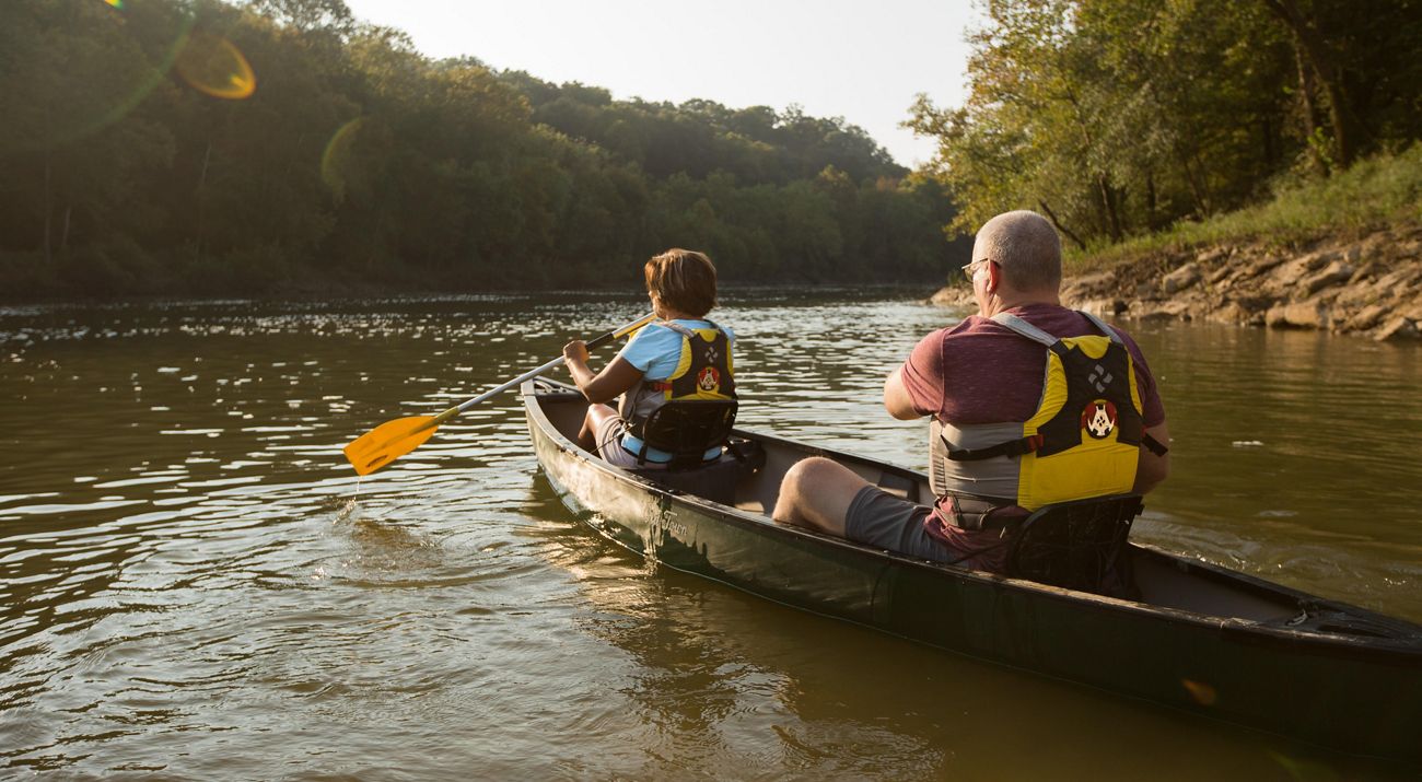 Two people canoe on a river.