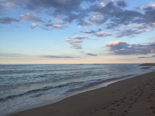 A view of the Atlantic ocean from the beach, with sand in the foreground and a partly cloudy sky at dusk in the background.