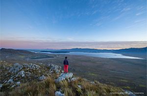 A person stands overlooking a vast landscape at dusk.