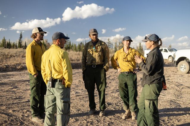 Five people in fire gear stand outside and talk to each other.