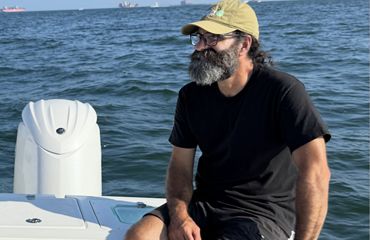 photo of Carl LoBue sitting on the edge of a boat with the ocean in the background.