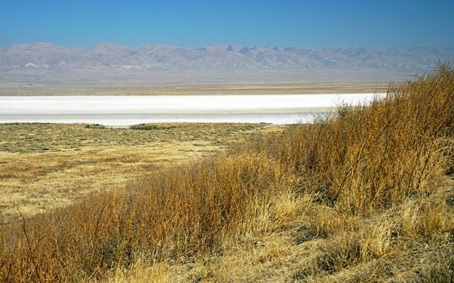 A white expanse of minerals on a dry lakebed with hills in the distance.