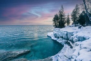 Icy and snow covered bank along Lake Superior under a sunset.