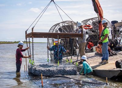 People in helmets working with oyster reef restoration equipment equipment in the water of Calcasieu Lake in Louisiana.