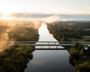 Sunrise over the Cape Fear River. Bridges carry cars across the river as white mist rises from the trees.