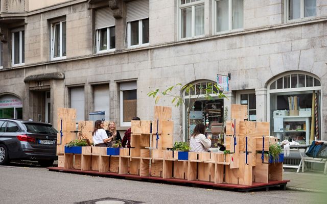 Personas sentadas conversando en un espacio cercado por cajas de madera donde crecen plantas.