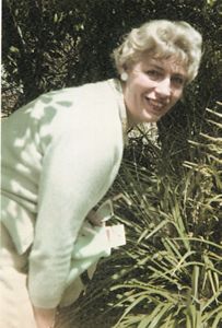 Portrait of Carolyn Aust, sharply dressed in a lush garden.