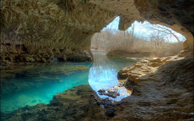 A cave opening with turquoise blue clear water in it.